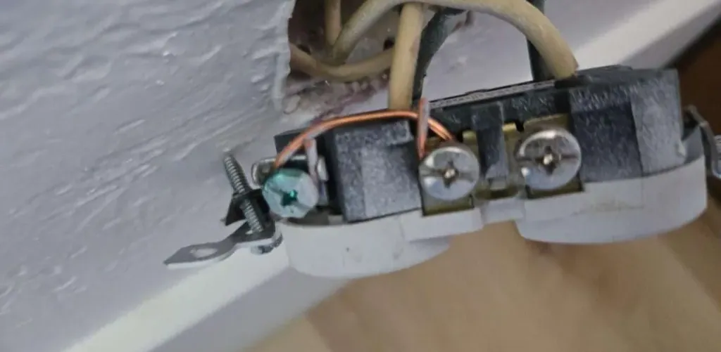Outlet with a copper jumper wire connecting the neutral and ground terminals, a classic bootleg ground