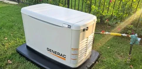 Generac whole-home standby generator on a pad with its gas connection beside a backyard fence